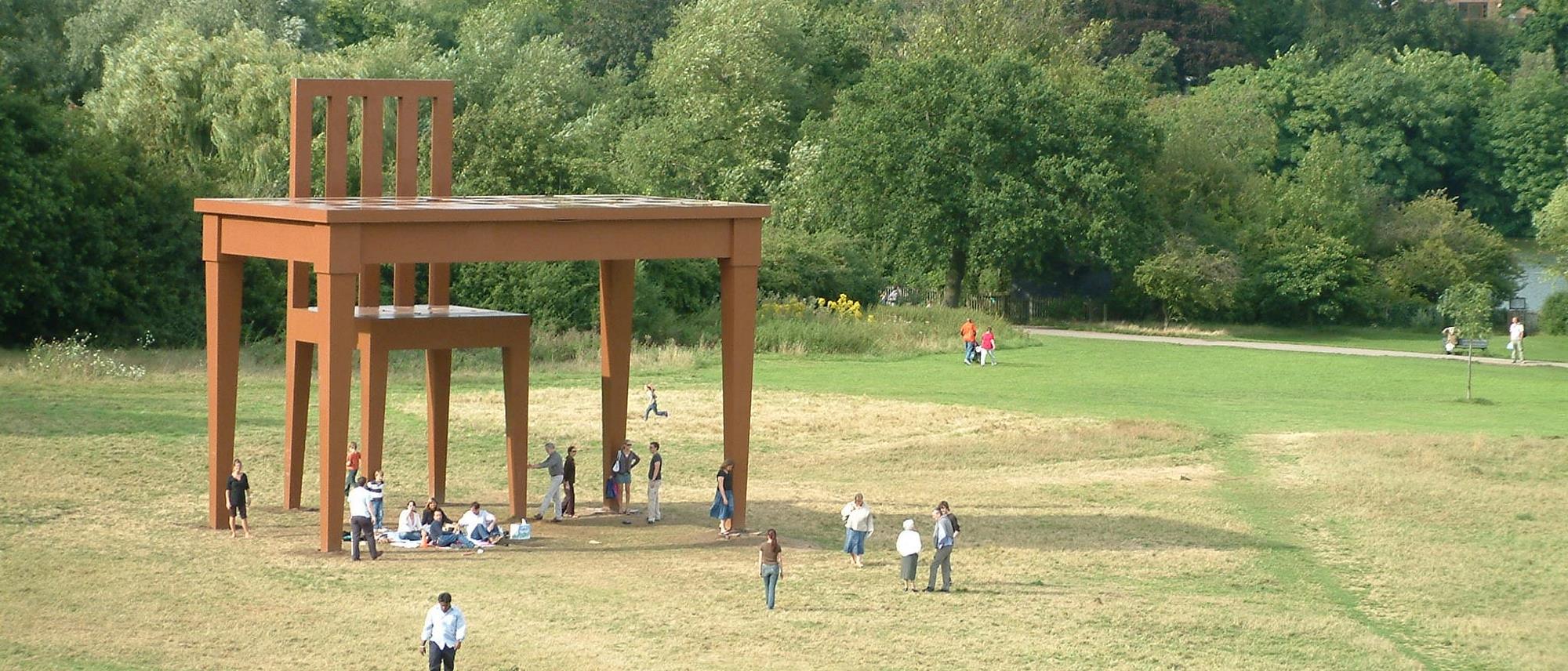 Huge table and chair in the park. People walking around 