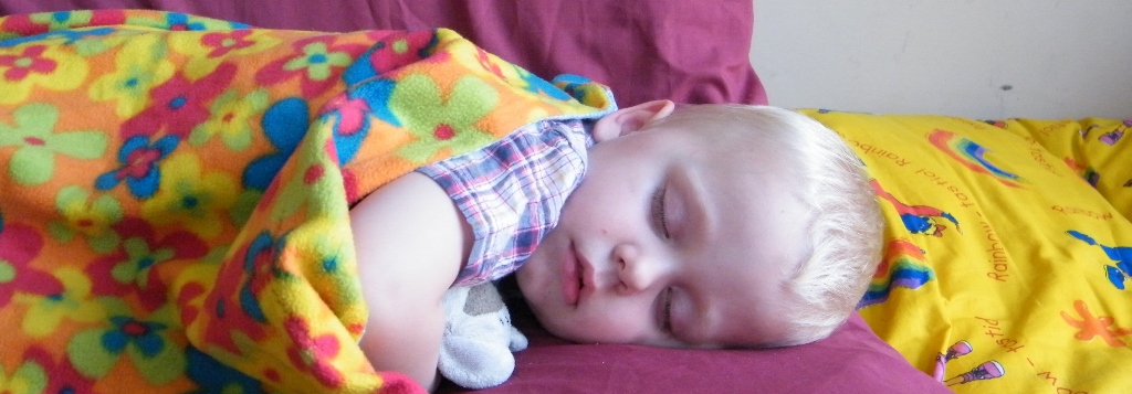 Little child sleeping on the sofa. Covered with colourful blanket 