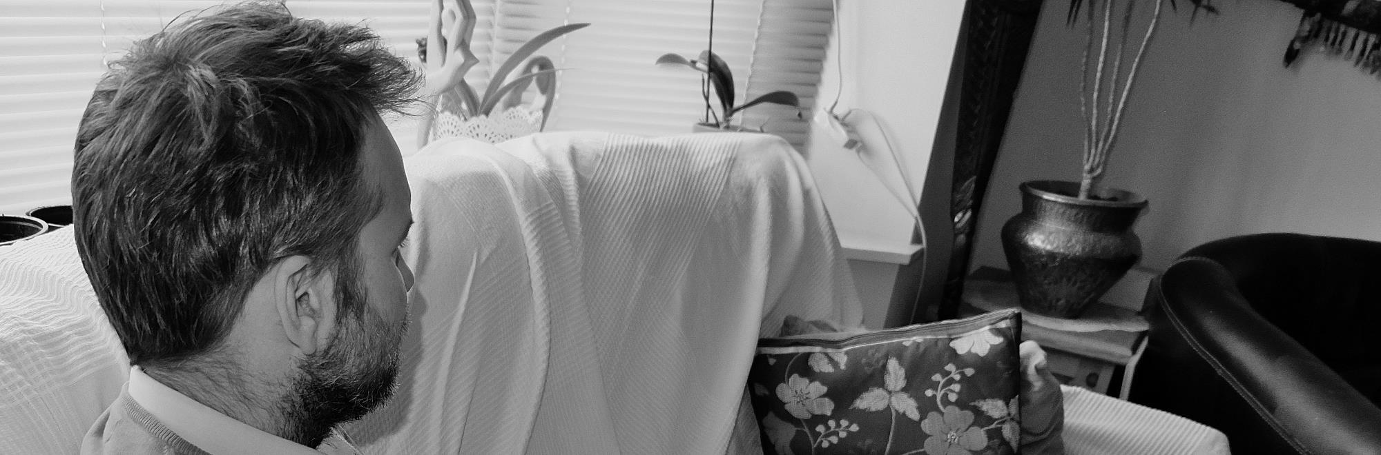 Man sitting on the sofa, turned to the side. Face can't be much seen. Black and white photo