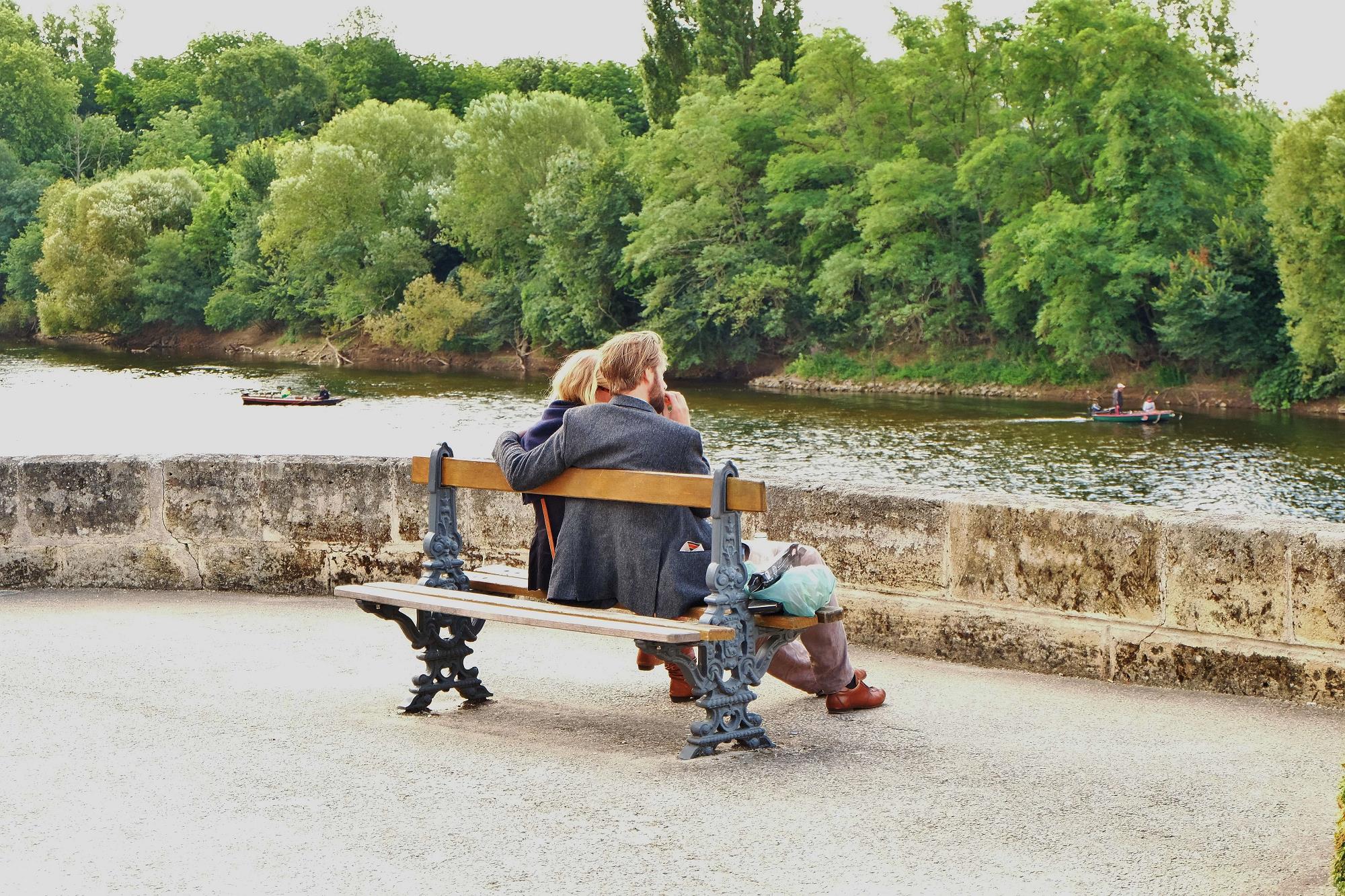 Couple is sitting on the bench, looking at the river and boats