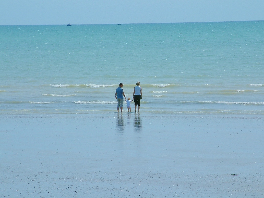 Man, woman and a little child between them. All holding hands, stepping in the sea